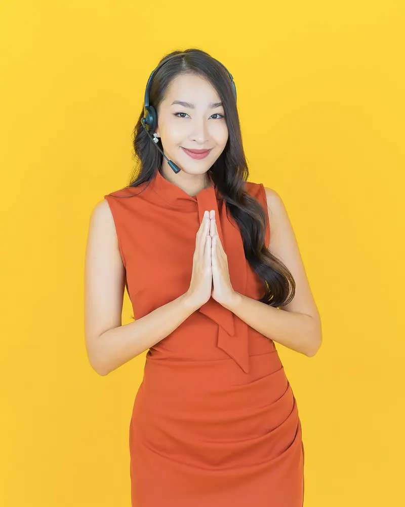 Seorang agen dukungan memakai headset tersenyum sambil menangkupkan kedua tangan sebagai salam.