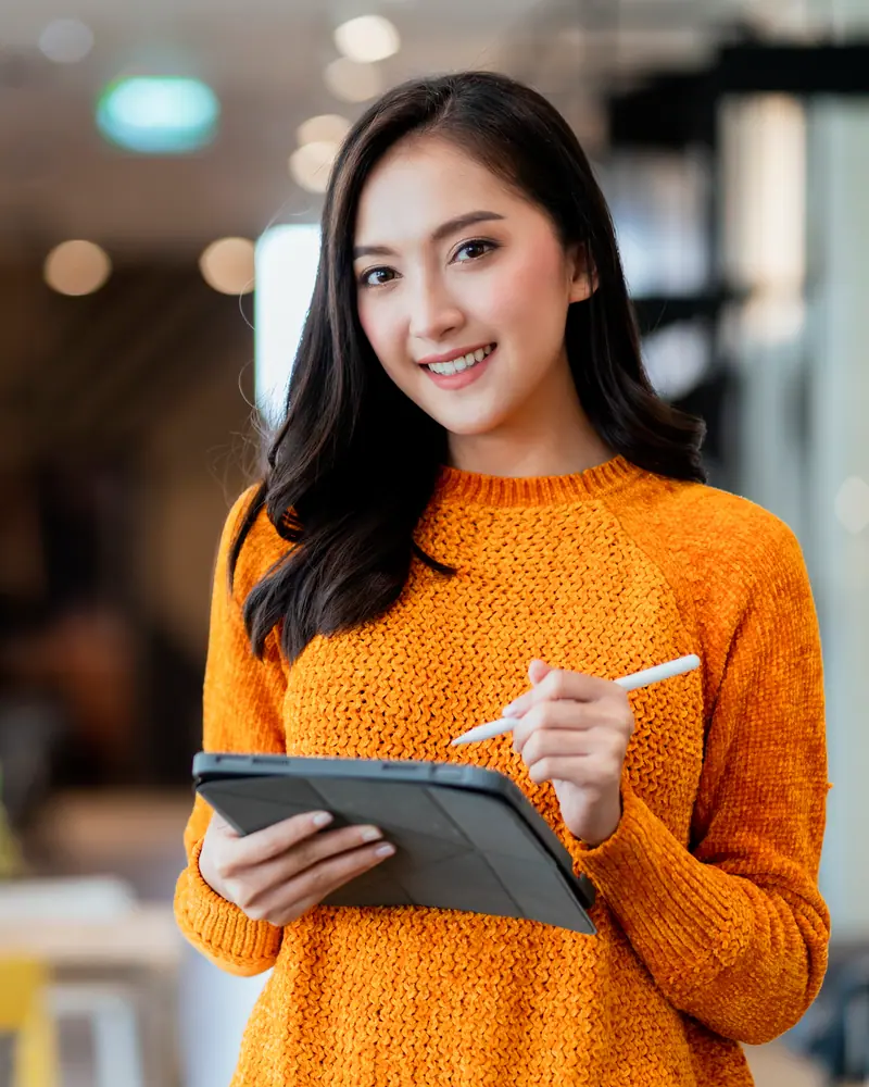 Seorang pemilik toko bersweter oranye tersenyum sambil memegang tablet dan stylus.